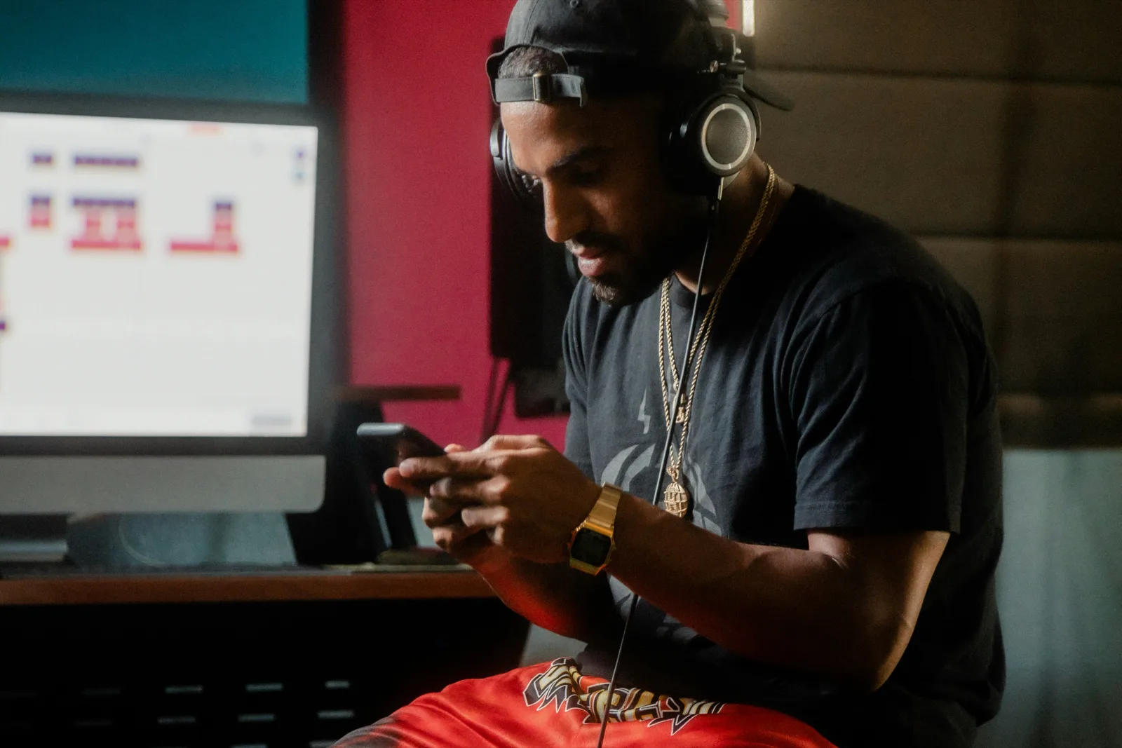 A writer in headphones reading his phone in a producer's room, a monitor with a track laid out behind him