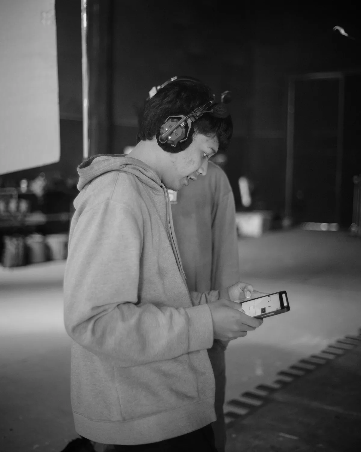 Side stage in black and white: a performer in headphones reading a piece off his phone